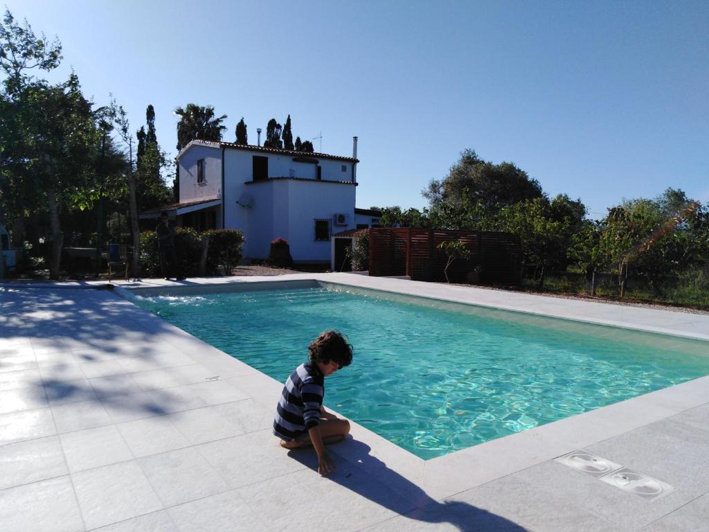 a young boy is sitting in front of a swimming pool at La Rucchetta - Alghero Villa e Depandance in Alghero