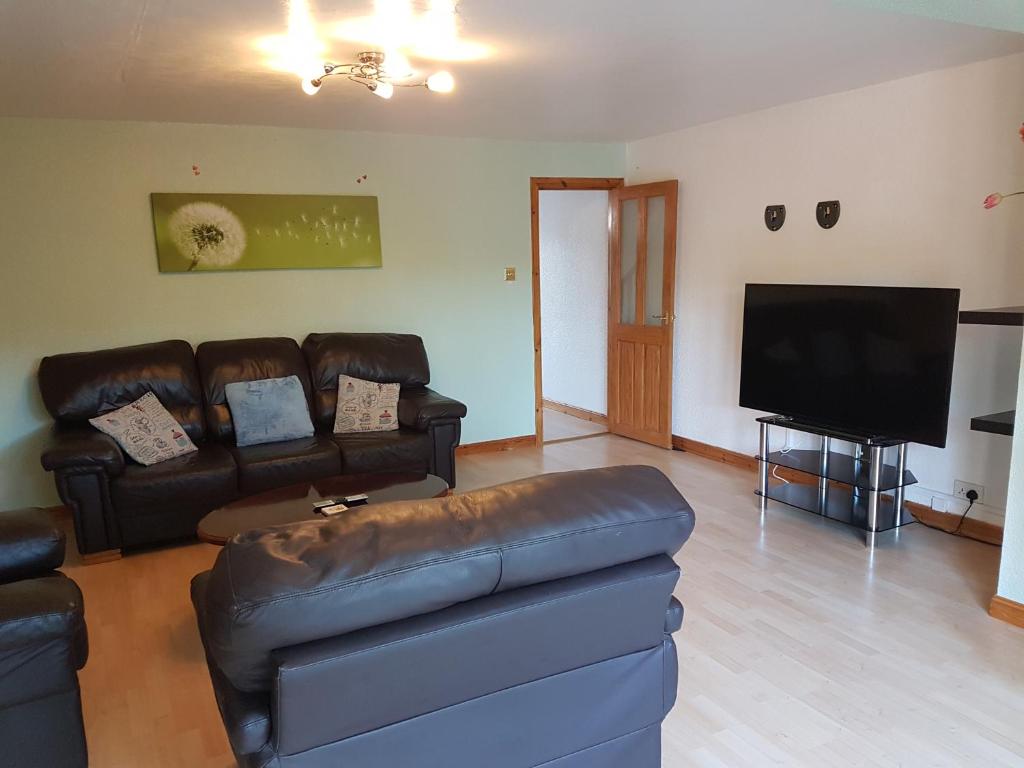 sala de estar con sofá de cuero y TV de pantalla plana en 3 bed room house en Aberdeen