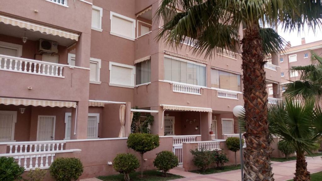 un edificio rosa con balconi bianchi e una palma di Apartamento en Arenals Del Sol ad Arenales del Sol