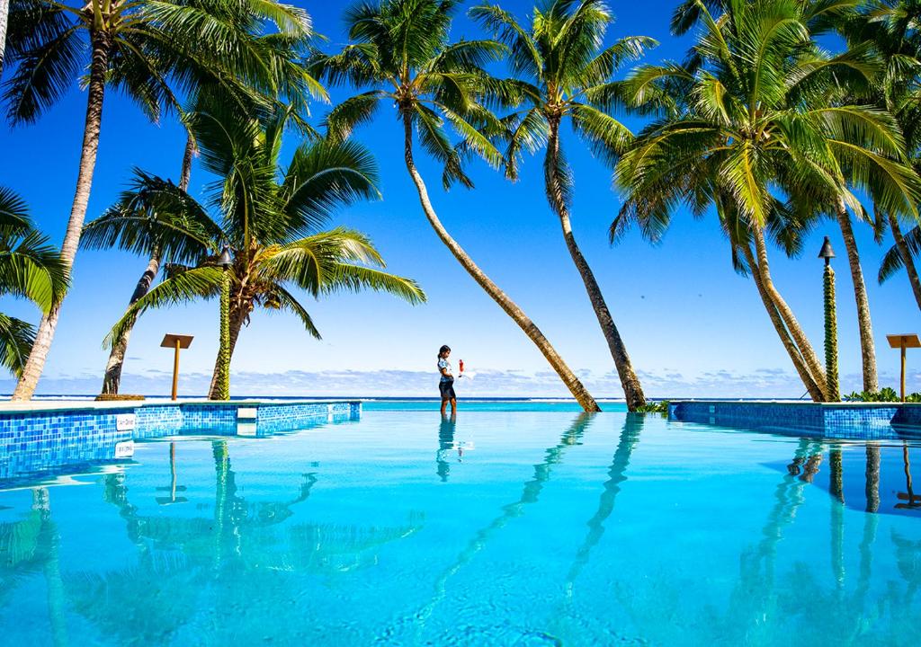 
a man standing on top of a blue surfboard in the ocean at Little Polynesian Resort in Rarotonga
