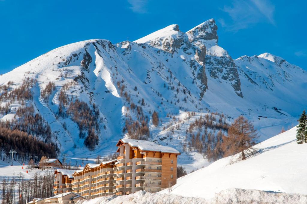 un bâtiment dans la neige devant une montagne dans l'établissement Résidence Plein Sud by Popinns, à La Foux