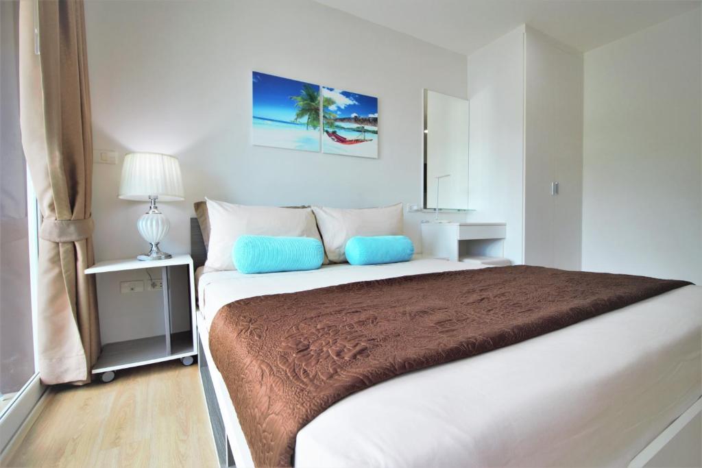 a white bedroom with a large bed with blue pillows at Ozone Condotel Kata Beach by PHR in Kata Beach