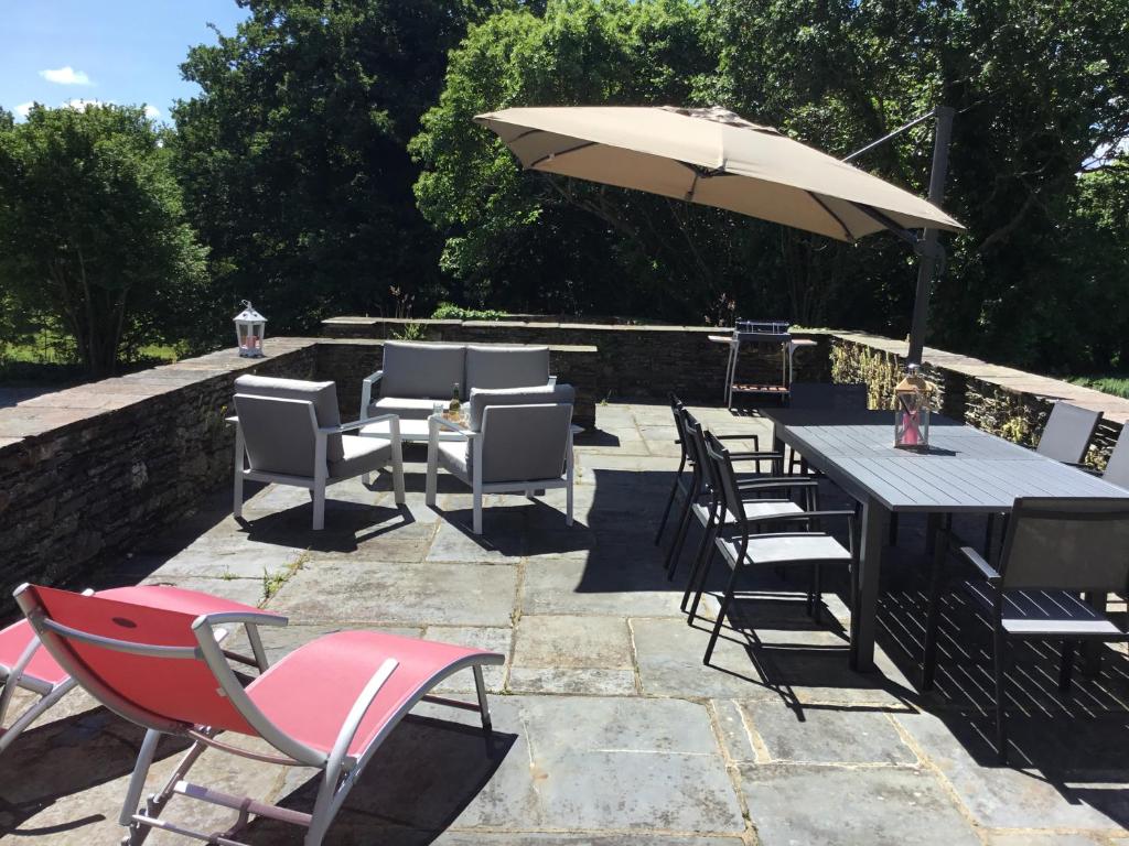 un patio con mesa, sillas y sombrilla en MANOIR DE BOTMINY LAC de GUERLEDAN en Caurel