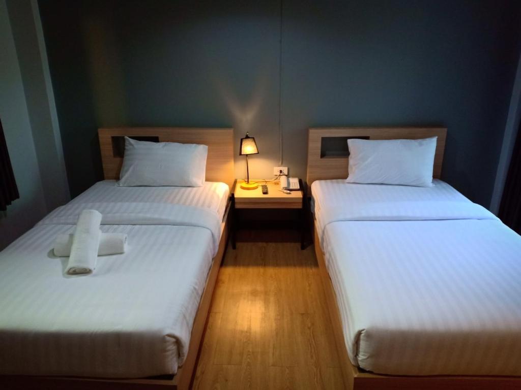 two beds in a room with a lamp and a table at บ้านเลขที่ 3 in Phitsanulok