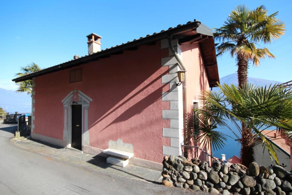a red building with a palm tree next to a street at Casa Lago Azzurro Apartement in Cannobio