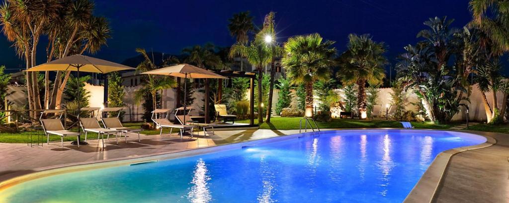 a swimming pool with chairs and umbrellas at night at Villa Araucaria in Partinico