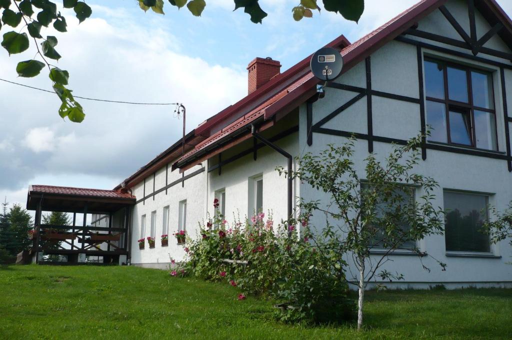 a white building with a red roof on a green field at Dylewianka in Wysoka Wieś