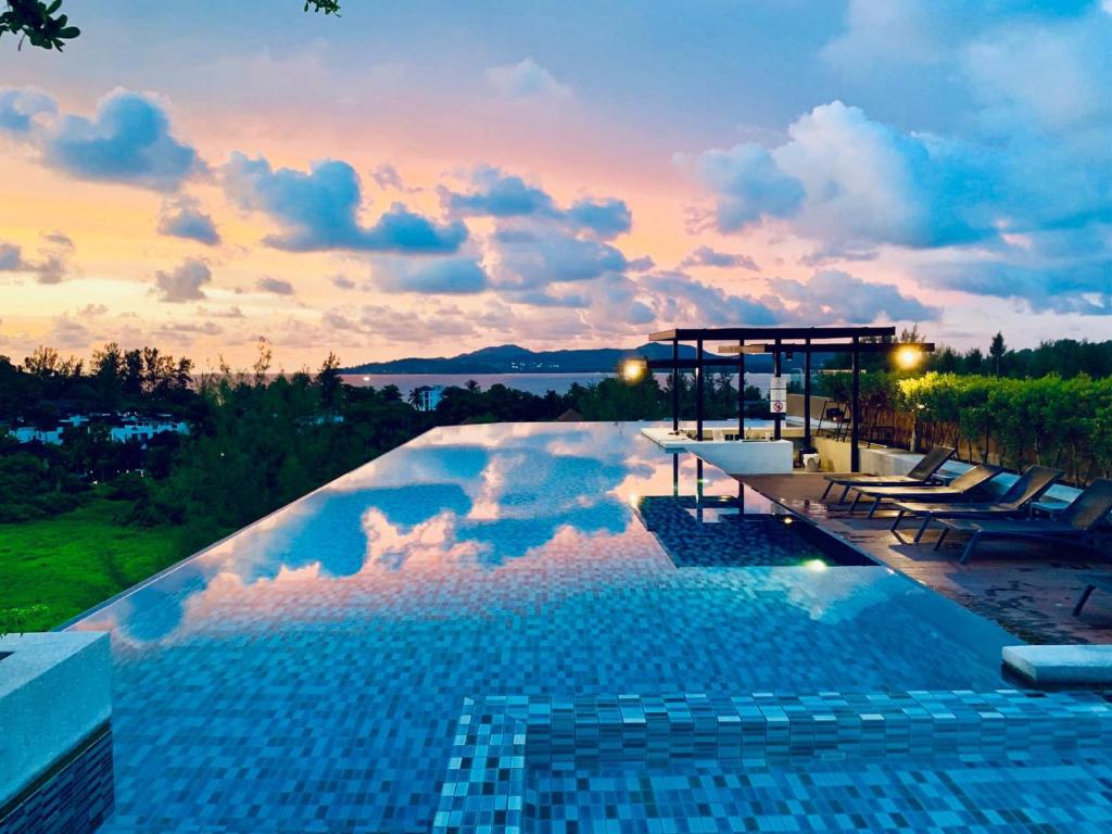 a swimming pool with a sunset in the background at 6th Avenue Surin by Lofty in Surin Beach
