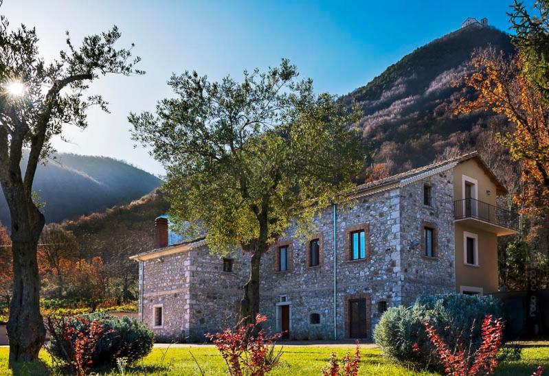 un bâtiment en pierre avec des arbres devant une montagne dans l'établissement Masseria boutique b&b, à Montella