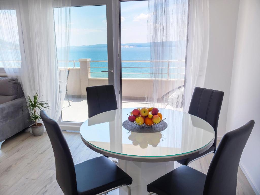 a dining room with a glass table with chairs and a bowl of fruit at Apartmani Ticinovic in Omiš