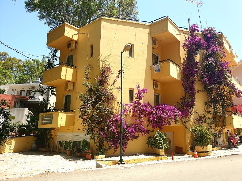 um edifício amarelo com flores roxas em Drosia Hotel em Georgioupolis