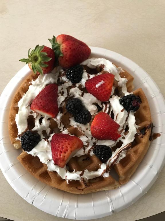 a waffle with strawberries and whipped cream and berries on a plate at Cozy Corner Motel in Williamstown