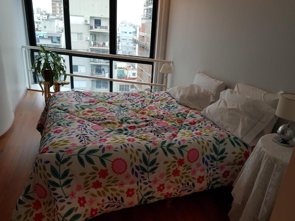 1 dormitorio con 1 cama con edredón de flores y ventana en Duplex Cabildo en Buenos Aires