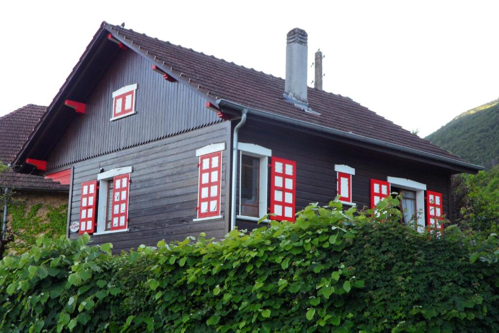 a black house with red windows and a hedge at Les Fougères in Sévrier