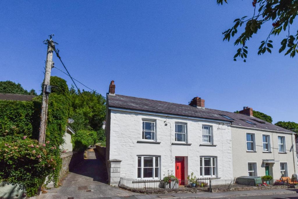 una casa blanca con una puerta roja en una calle en Bwthyn y Bardd, en Llanstephan