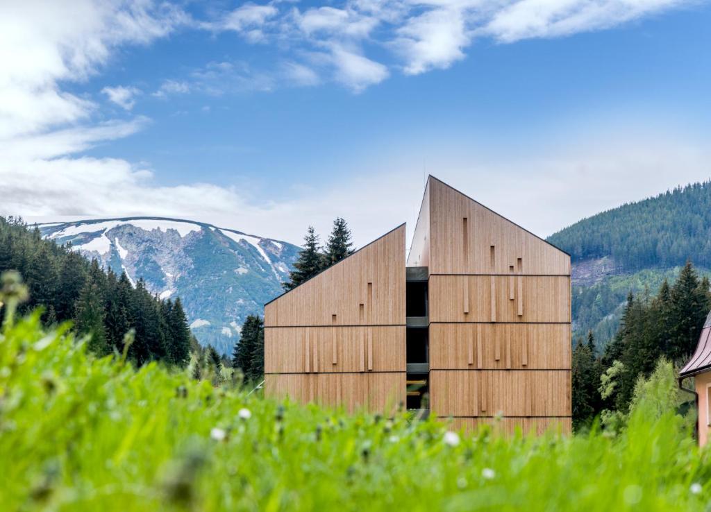 drewniany budynek na wzgórzu z górami w tle w obiekcie HOTEL PECR DEEP w mieście Pec pod Sněžkou