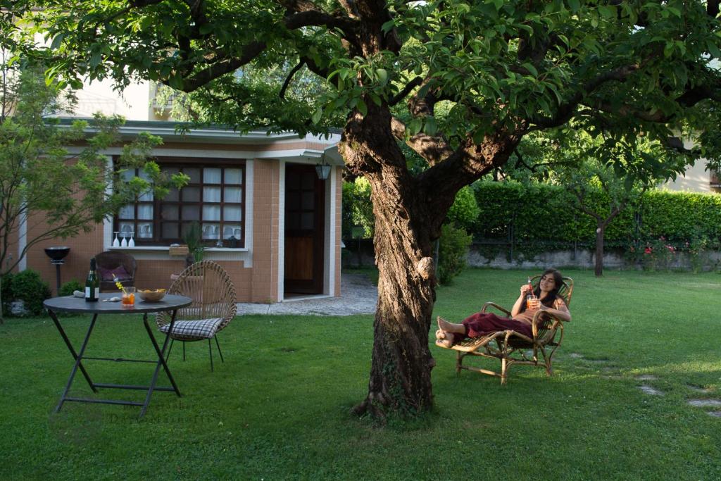 a woman sitting in a chair next to a tree at Casetta del Molo in Mandello del Lario