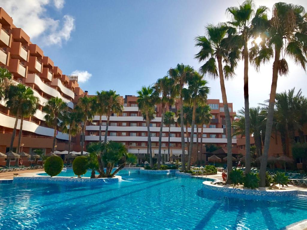 a swimming pool with palm trees in front of a hotel at Arena Center in Roquetas de Mar