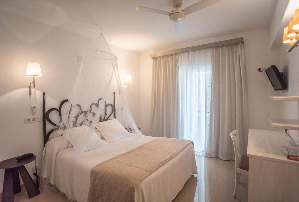 a white bedroom with a large bed and a window at Hotel Sa Volta in Es Pujols