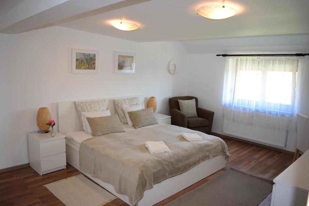 a white bedroom with a large bed and a chair at Pensiunea Corbeanca - cazare si evenimente in Corbeanca