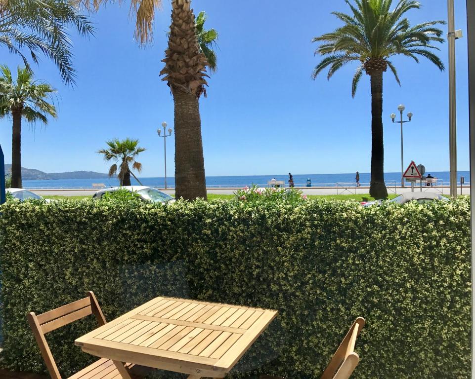 a wooden table and chairs with palm trees and the beach at Sea View- Easy Home Booking in Nice