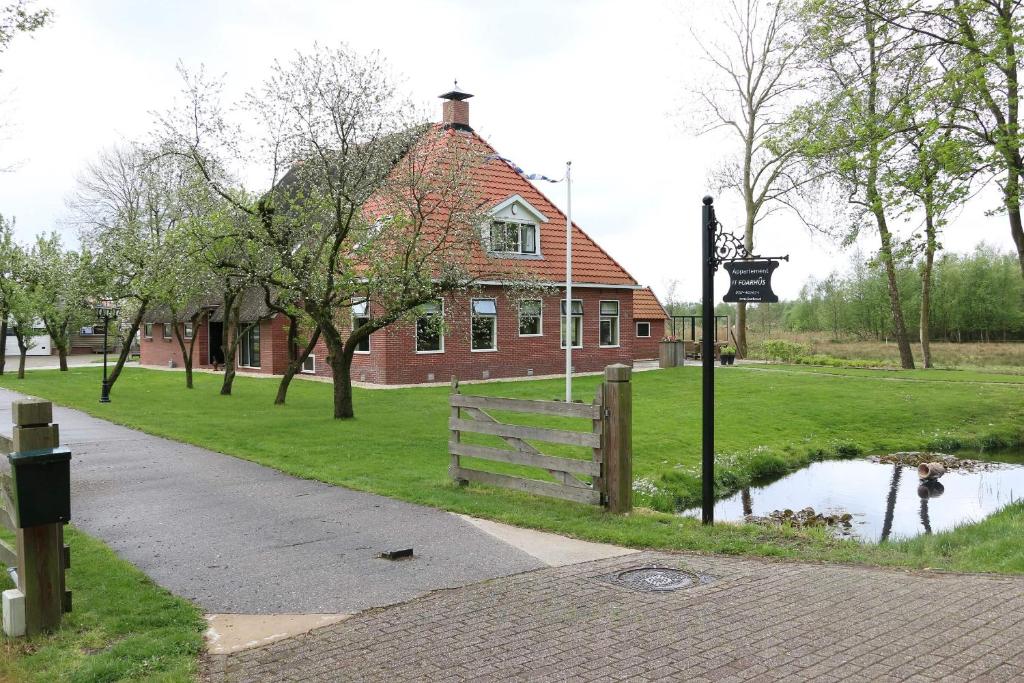 ein Backsteinhaus mit einem Zaun und einem Teich davor in der Unterkunft It Foarhús in Eernewoude