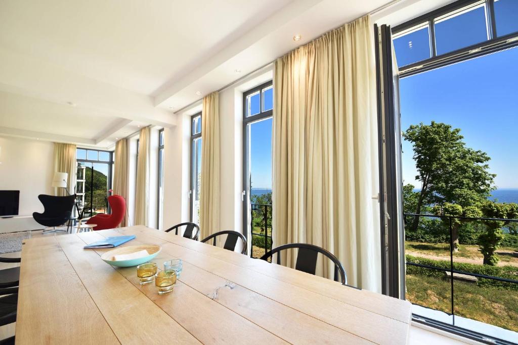 een eetkamer met een houten tafel en grote ramen bij Luxus Apartment Küstenblick in Ostseebad Sellin