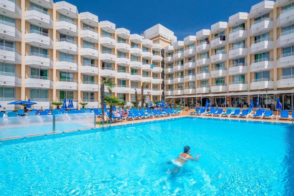 Ein Mann schwimmt im Pool vor einem Hotel. in der Unterkunft GHT Oasis Tossa & Spa in Tossa de Mar