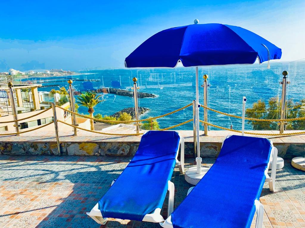 a pair of blue chairs and an umbrella on a balcony at First Line Seaview Apartment in Adeje