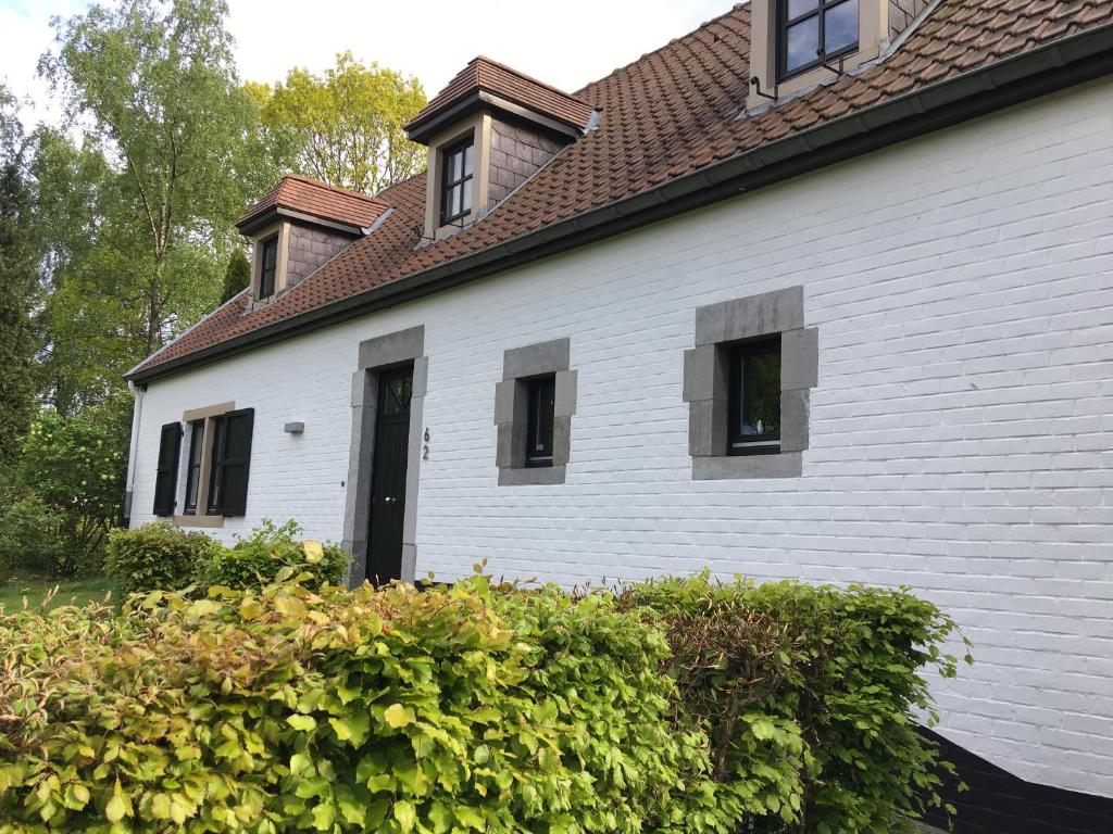 a white house with a black door and some bushes at La dreve in Verviers