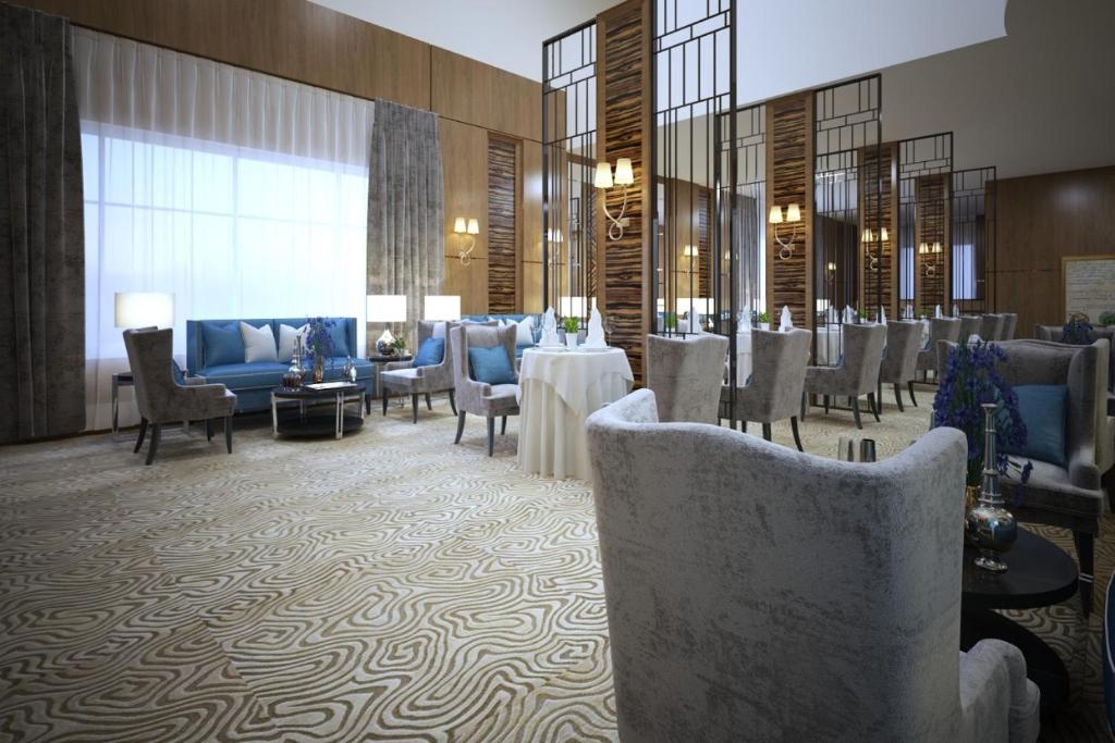 a hotel lobby with chairs and tables and a dining room at Lavona Tiba Hotel in Dammam