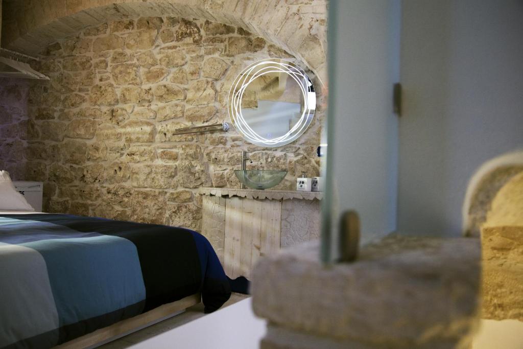 1 dormitorio con pared de piedra, cama y espejo en Vico Santa Maria en Putignano