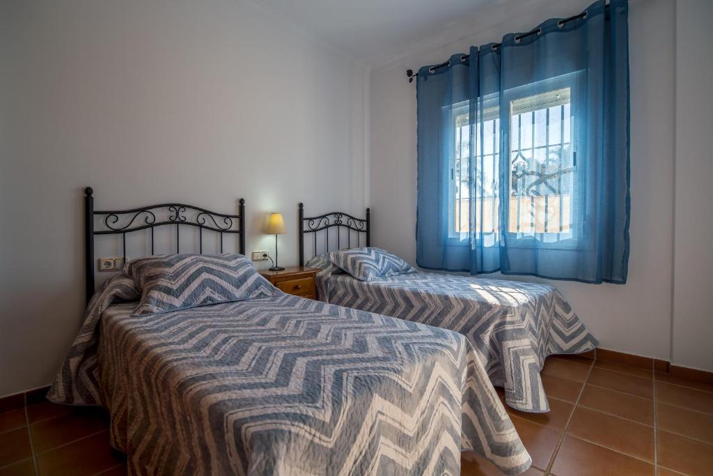 sypialnia z 2 łóżkami i oknem z niebieskimi zasłonami w obiekcie Chalet adosado Atalaya P w mieście Conil de la Frontera