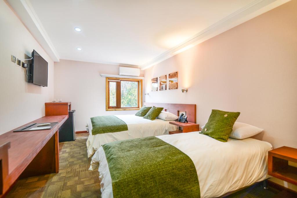 Una habitación de hotel con dos camas y un escritorio. en Hotel Pucón Indómito, en Pucón