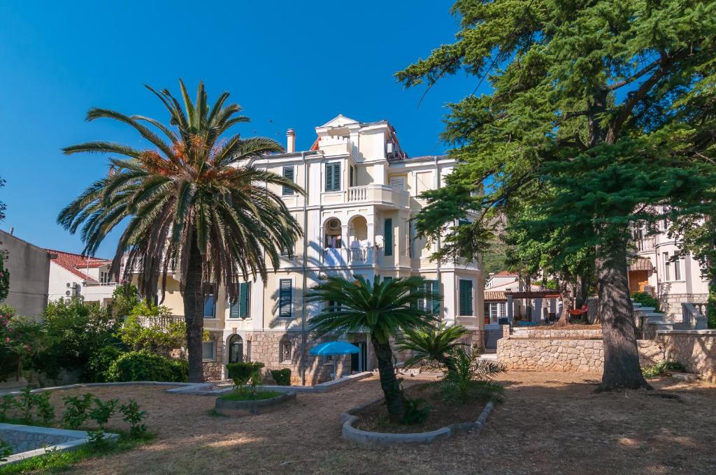 a large white house with palm trees in front of it at Apartments Carmen & Tosca in Dubrovnik