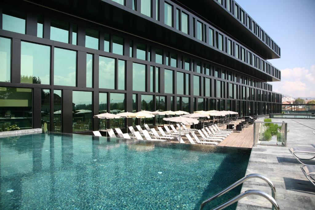 uma piscina em frente a um edifício com cadeiras e guarda-sóis em Axis Viana Business & SPA Hotel em Viana do Castelo