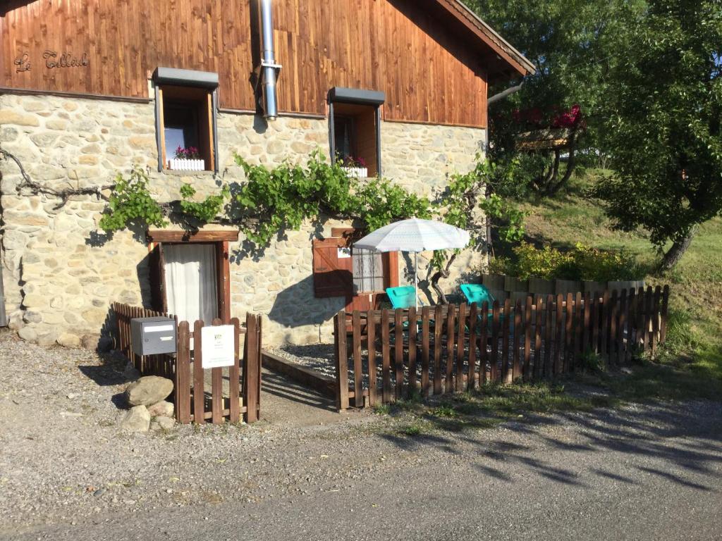 uma cerca de madeira com um guarda-sol e cadeiras em frente a um edifício em Gîte Le Tilleul 1* em Fouillouse