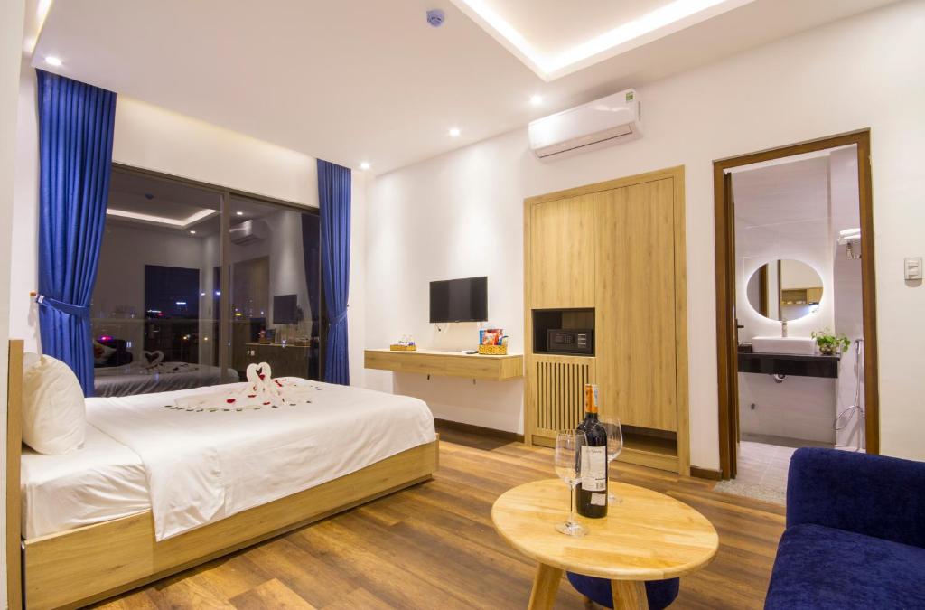 A staged bedroom with a city-facing window, desk, television and adjoining bathroom.