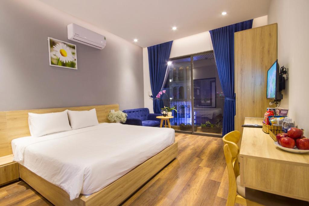A bright bedroom pairs a wood-framed bed with a desk, television, and curtained window.