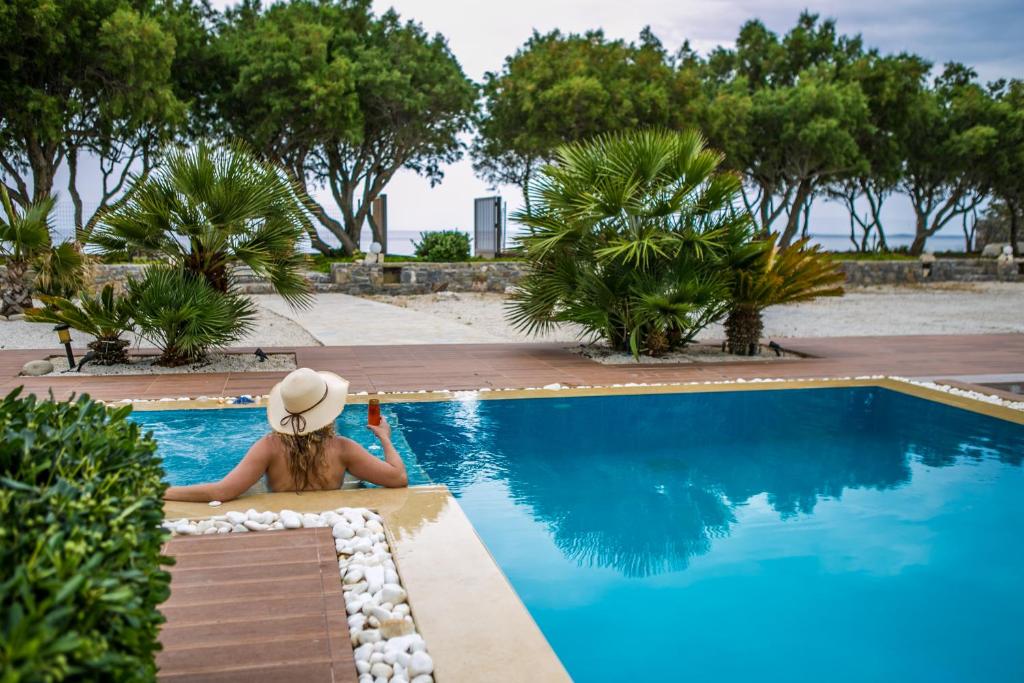 una mujer con sombrero sentada junto a una piscina en Villa Pelagos, en Koutsounari