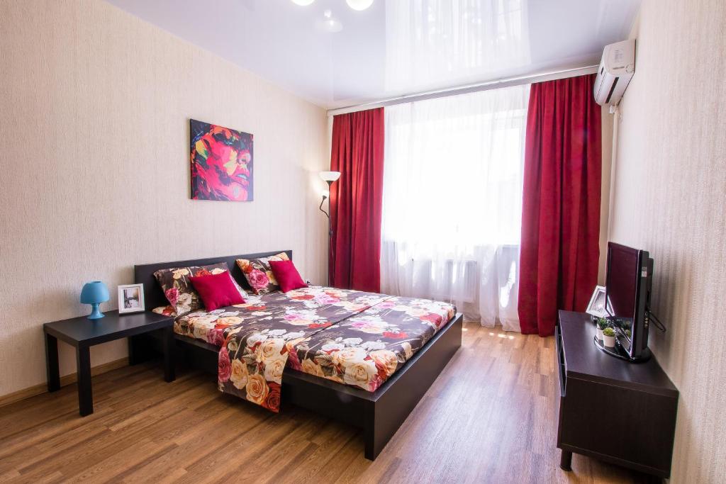 クラスノダールにあるАпартаменты у Парка Краснодар на Восточно-Кругляковскойのベッドルーム1室(ベッド1台付)、赤いカーテン付きの窓が備わります。