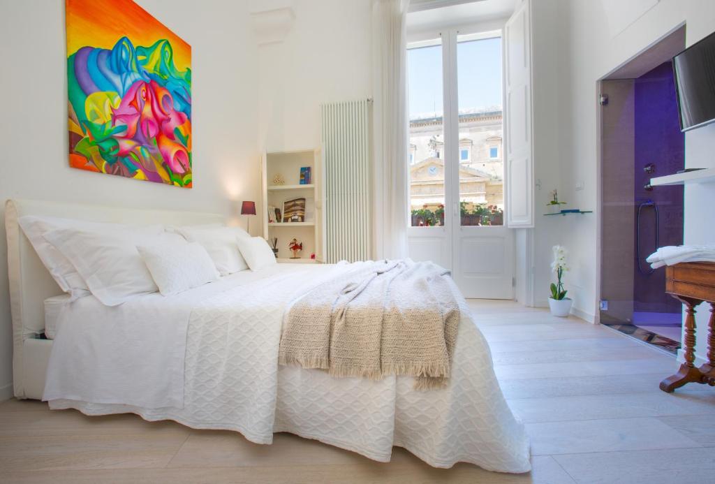 a bedroom with a white bed with a painting on the wall at La Finestra sul Convitto B&B in Lecce