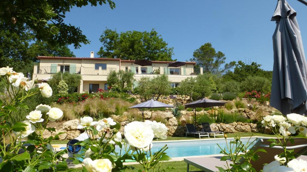 een huis met een zwembad en een parasol en bloemen bij Le Vallon des Oliviers in Montauroux