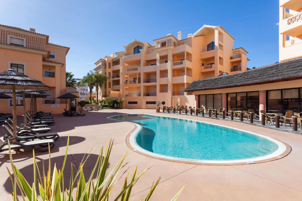 una piscina en un complejo con sillas y un edificio en Aum Praia da Luz Resort Apartment, en Luz