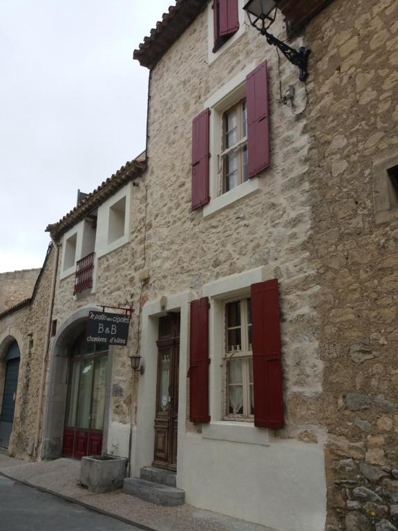 un edificio de piedra con persianas rojas en una calle en Le Patio Des Cigales, en Roquefort-des-Corbières