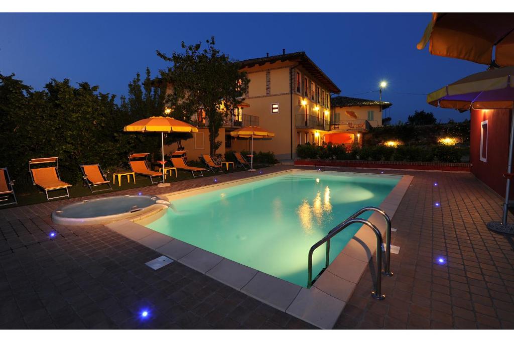 a swimming pool at night with chairs and umbrellas at Agriturismo Bianconiglio in Monforte dʼAlba