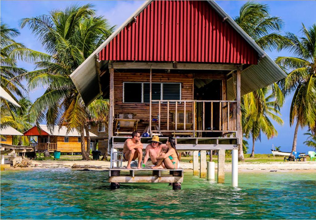 tres personas sentadas en el muelle de una casa en el agua en Private Cabin Over the Water PLUS Meals - San Blas Islands - private bathroom, en Panamá