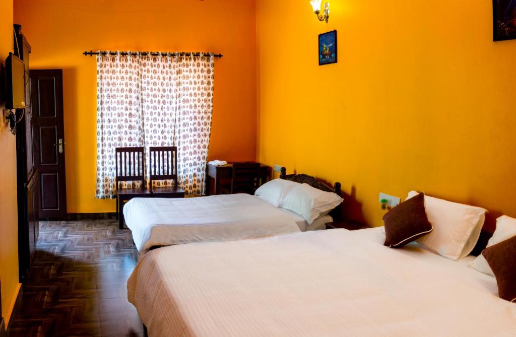 2 Betten in einem Zimmer mit gelben Wänden und einem Fenster in der Unterkunft Sharanyam Homestay in Mananthavady
