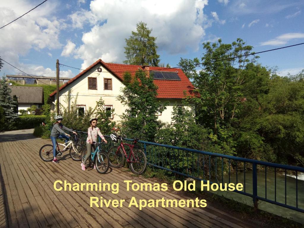 two people riding bikes on a bridge in front of a house at Tomas Old House - River Apartments in Visoko