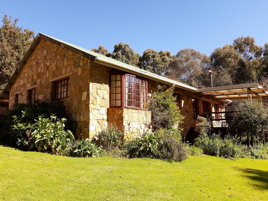 a stone house with a grass yard in front of it at Crane Cottage in Dullstroom